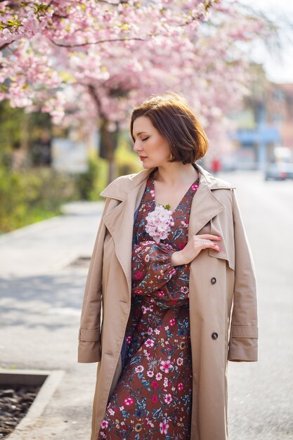 Portret van een zachte vrouw tegen de achtergrond van sakura bloemen. Loop in de bloeiende sakura-tuin. Jonge stijlvolle vrouw die in het Sakura-park staat en geniet van schoonheid