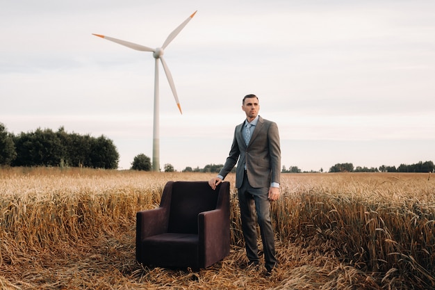 Portret van een zakenman in een grijs pak en stropdas, staande in de buurt van een stoel in een tarweveld. europa.