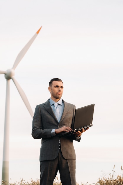 Portret van een zakenman in een pak met een laptop in een tarweveld tegen de achtergrond van een windmolen en de avondlucht