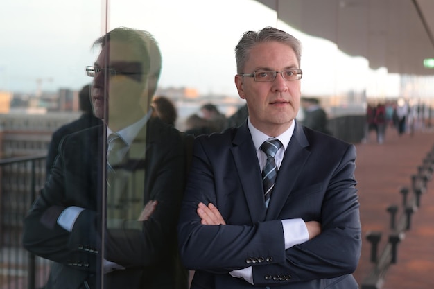 Portret van een zakenman met gekruiste armen die buiten op glas leunt
