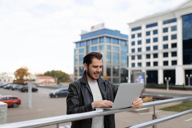 Portret van een zakenman op de achtergrond van stadskantoorgebouwen die online op een laptop werken