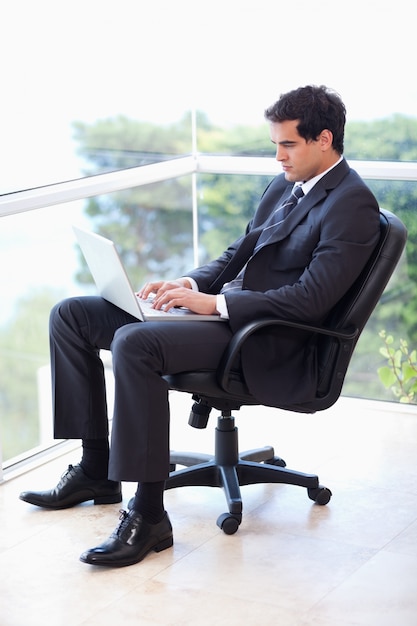 Portret van een zakenman zittend op een leunstoel werken met een laptop