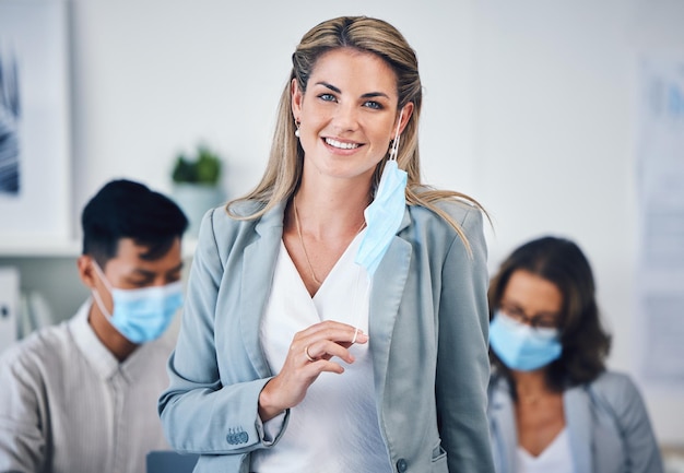 Portret van een zakenvrouw in haar kantoor met een gezichtsmasker en haar team tijdens covid pandemie Corporate creatieve en professionele manager die werkt aan een groepsproject in de vergaderruimte van het bedrijf