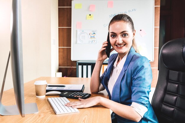 Portret van een zakenvrouw met een mobiele telefoon die aan een bureau in het kantoor zit