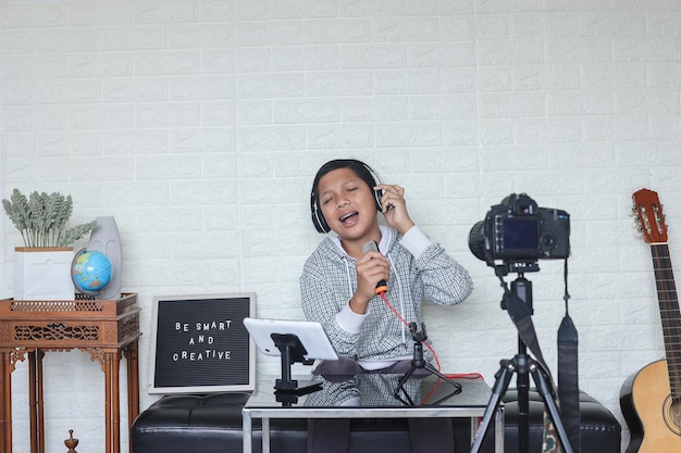 Portret van een zelfverzekerd en creatief Aziatisch kind dat op de camera zingt en muziekdekking maakt. Online invloed