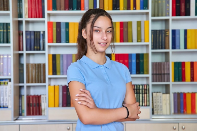 Portret van een zelfverzekerd tienerschoolmeisje dat naar de camera in de bibliotheek kijkt