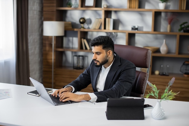 Portret van een zelfverzekerde bebaarde man die thuis met een laptop aan een project werkt