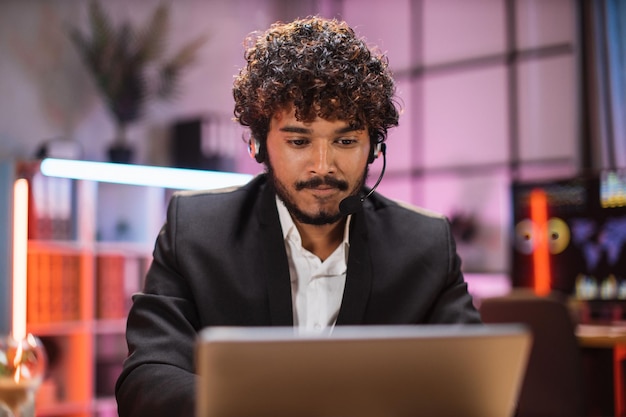 Portret van een zelfverzekerde bebaarde man in formele kleding en headset die op kantoor werkt met een laptop