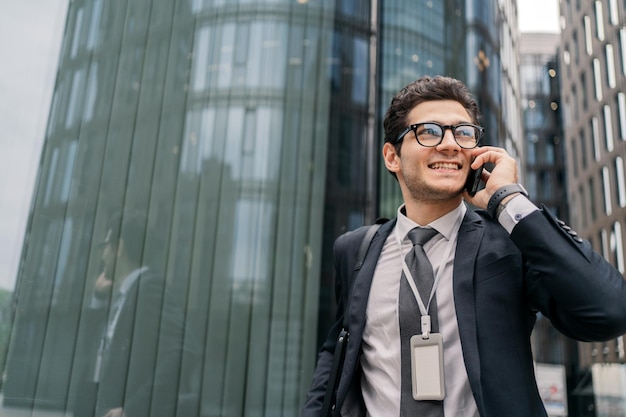 Portret van een zelfverzekerde man die lacht, praten aan de telefoon in een pak met bril