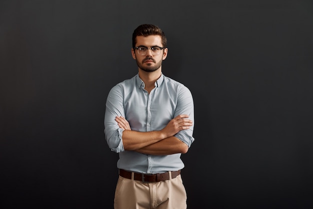 Portret van een zelfverzekerde, serieuze jonge bebaarde man die naar de camera kijkt en zijn armen gekruist houdt terwijl