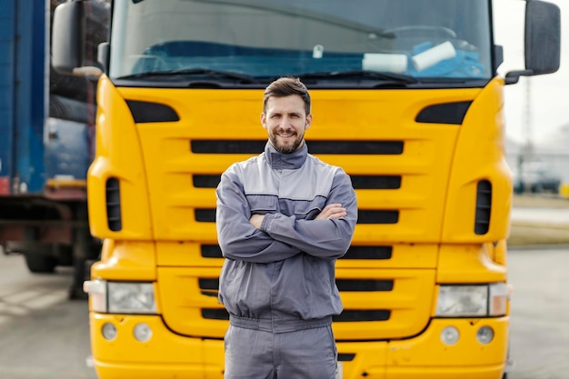 Portret van een zelfverzekerde vrachtwagenchauffeur die naar de camera glimlacht terwijl hij voor de vrachtwagen staat