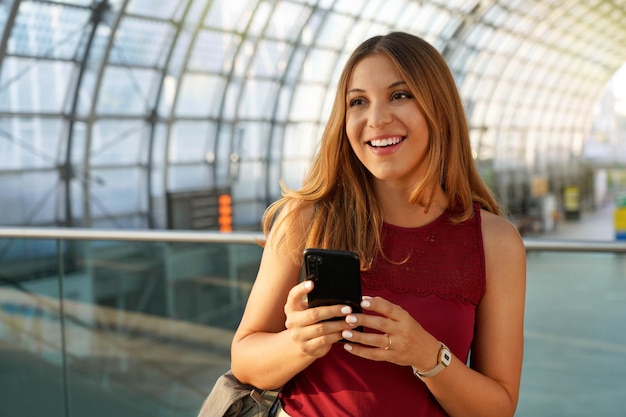 Portret van een zelfverzekerde vrouw die naar de zijkant kijkt en een smartphone vasthoudt in de moderne luchthaven. Ruimte kopiëren.