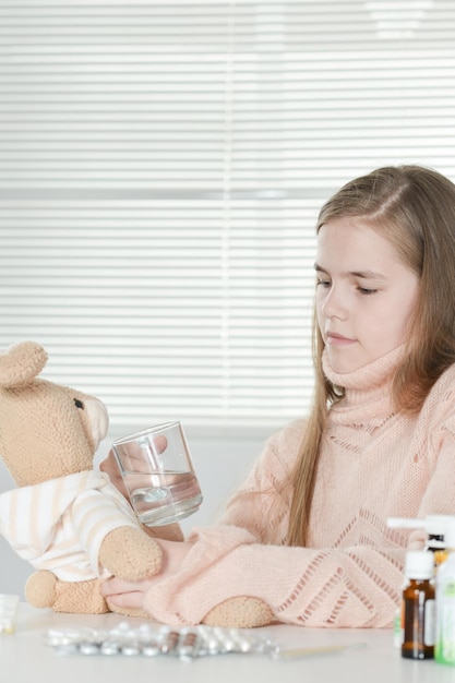 Portret van een ziek meisje dat verpleegster speelt met konijnenspeelgoed terwijl ze thuis aan tafel zit met medicijnen