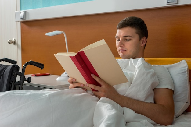 Portret van een zieke mannelijke patiënt die in het ziekenhuisbed ligt en een boek leest op de ziekenhuisafdeling. Zorgconcept