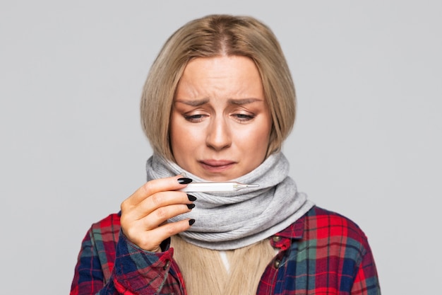 Foto portret van een zieke vrouw die de thermometer bekijkt om haar temperatuur te controleren