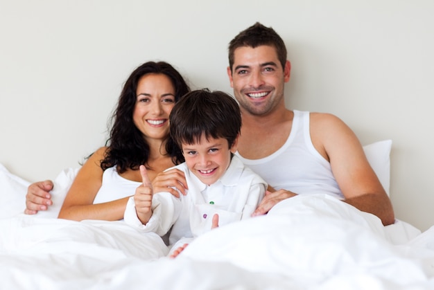 Portret van een zoon met duimen omhoog en zijn ouders in bed