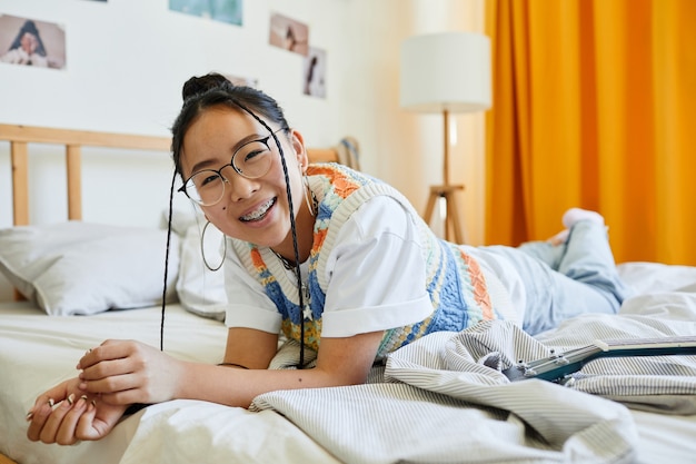 Portret van een zorgeloos tienermeisje dat op bed in een gezellige kamer ligt en naar de camera kijkt