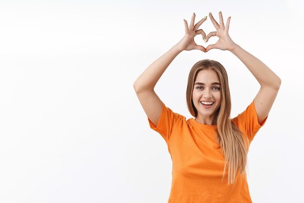 Portret van een zorgeloze, aantrekkelijke blanke vrouw met blond haar die handen boven het hoofd opsteekt en de liefde bedreef, hartgebaar