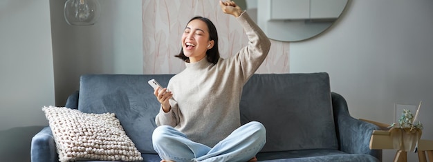 Portret van een zorgeloze aziatische vrouw die draadloos muziek zingt en luistert vanaf de smartphone-app
