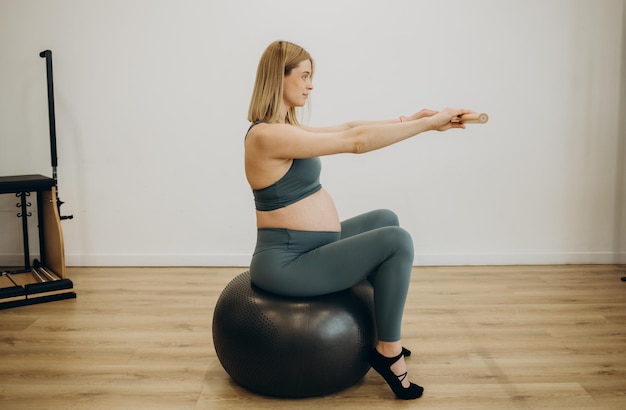 Portret van een zwangere vrouw die oefeningen doet met halters op een fitnessbal geïsoleerd op een witte achtergrond