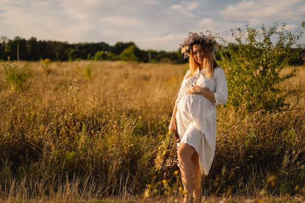 Portret van een zwangere vrouw een mooie jonge zwangere vrouw in een witte jurk loopt in het veld