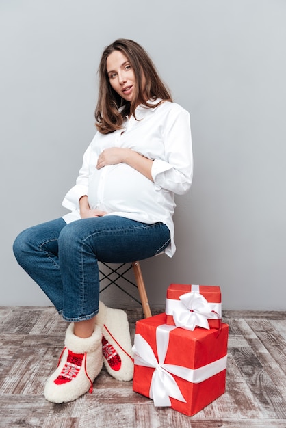 Portret van een zwangere vrouw met geschenken van volledige lengte zittend op een stoel in de studio