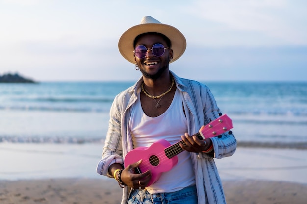 Portret van een zwarte etnische man geniet van de zomervakantie op het strand en speelt ukelele