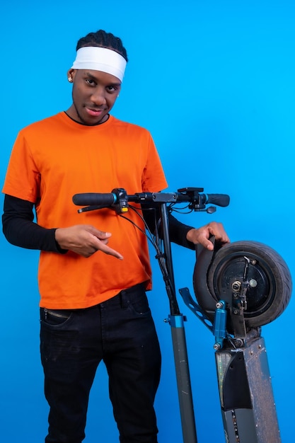 Portret van een zwarte etnische man in oranje kleding op een blauwe achtergrond met een lachend elektrisch skateboard