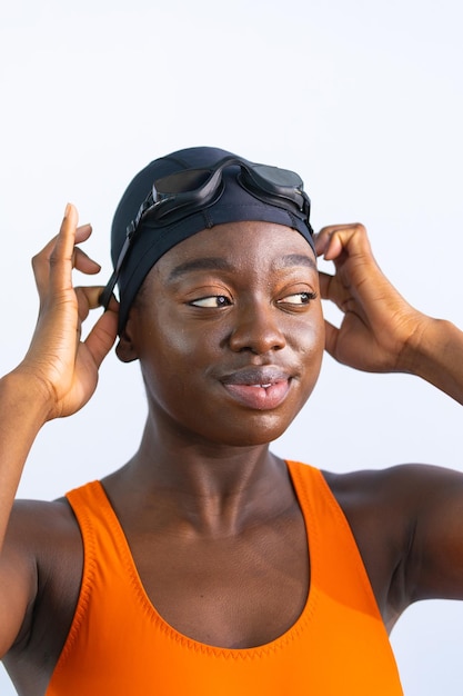 Portret van een zwarte jonge vrouw die glimlacht terwijl ze haar zwembril en effen witte achtergrond aanpast