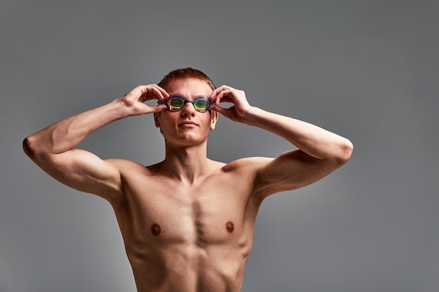 Portret van een zwemmer in een pet en masker, portret van halve lengte, jonge atleet zwemmer die een pet en masker draagt om te zwemmen, kopieën van ruimte, grijze achtergrond