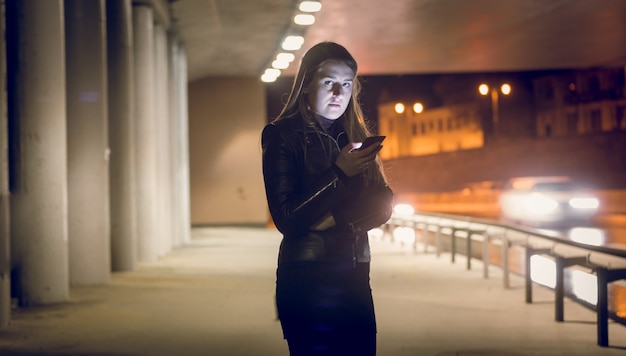 Portret van eenzame vrouw die een sms-bericht typt op de donkere straat
