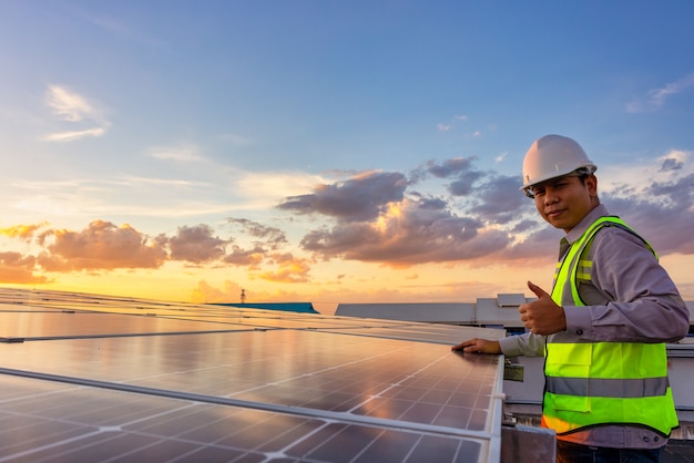 Portret van elektricien in veiligheidshelm en uniform op achtergronddak van fotovoltaïsche zonnepanelen. Mannelijke technicus bij zonnestation.