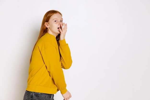 Portret van emotioneel tienermeisje in gele trui poseren geïsoleerd over witte studio achtergrond