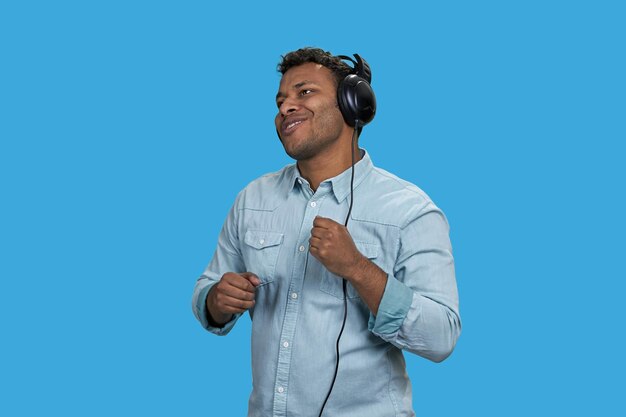 Portret van emotionele bruine Indiase man genieten van muziek in koptelefoon geïsoleerd op blauwe achtergrond