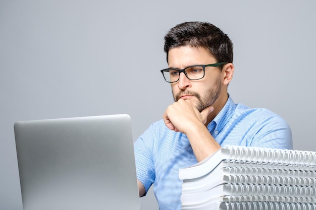 Portret van ernstige geconcentreerde man aan het werk op laptop en zittend aan de tafel geïsoleerd op grijs
