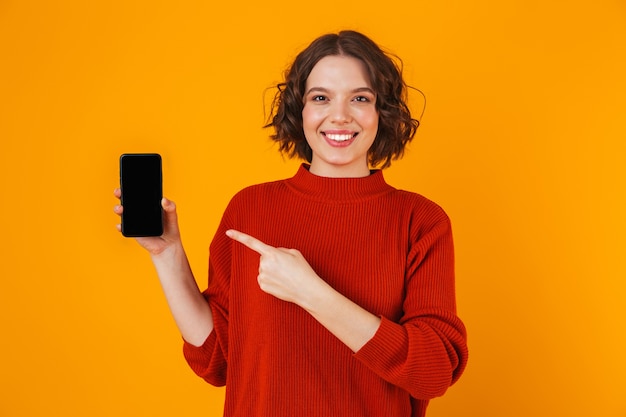 Portret van Europese vrouw 20s die sweater dragen die smartphone houden en demonstreren terwijl status geïsoleerd over geel