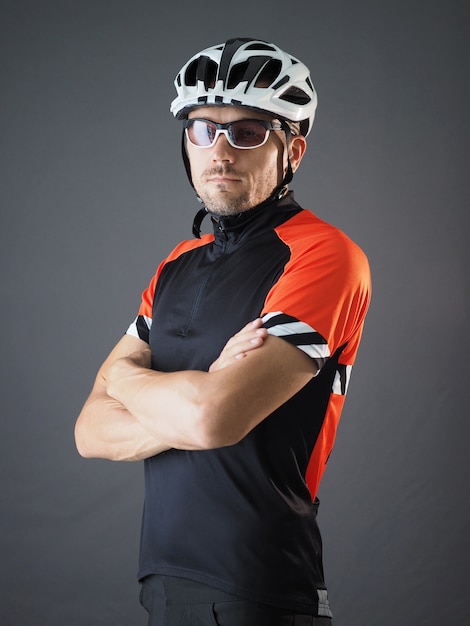 Portret van fietser met handen gekruiste borst die witte helm en sporttrui draagt.