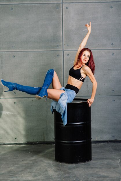 Portret van fitness vrouw op cement betonnen achtergrond, in de buurt van een zwart vat.