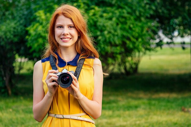 Portret van fotosessie professionele mooie jonge gember roodharige Ierse meisje in een gele jurk gefotografeerd in het zomerpark. fotograaf in fotoshoot met een grote camera en een gave lens