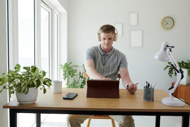 Portret van freelancer in hoofdtelefoon kijken naar productpresentatie op tablet pc