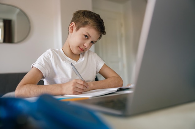 Foto portret van geconcentreerde jongen met laptop die huiswerk maakt en thuis schrijft