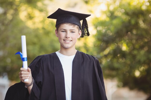 Portret van gediplomeerde schooljongen die zich met graadrol in campus bevindt