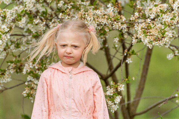 Foto portret van gefrustreerd of boos klein meisje buiten bij een bloeiende boom met een grappige grimace op haar gezicht