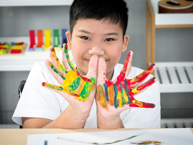 Portret van gehandicapt kind in de rolstoel laat zijn handen zien die trots zijn geschilderd in het ruimtelijke klaslokaal