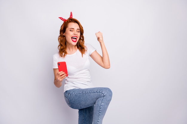 Portret van gekke vrolijke vrouw wint loterij sociale media, steekt vuisten op, schreeuw ja, draag jeans t-shirt geïsoleerd over witte kleur muur