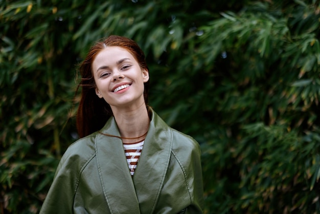 Portret van geluk vrouw met rood vliegend haar glimlach met tanden wandelen in de stad in het park tegen een achtergrond van groene bamboe bladeren lente in de stad