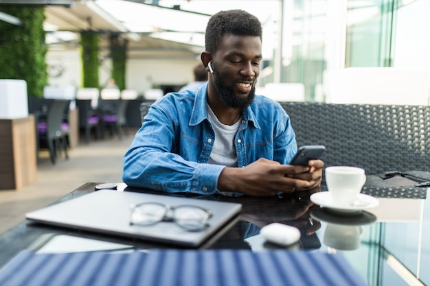 Foto portret van gelukkig afrikaanse zakenman met behulp van telefoon tijdens het werken op laptop in een restaurant