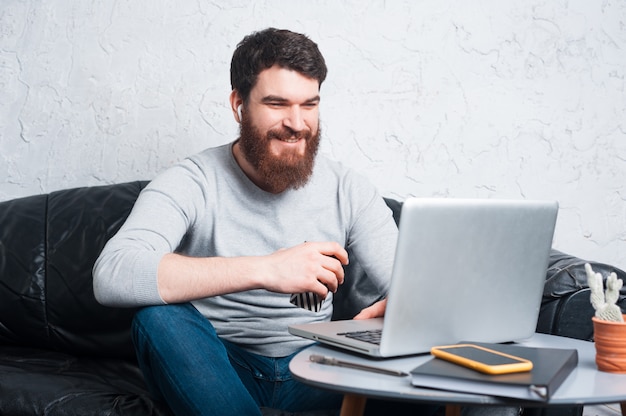 Portret van gelukkig bebaarde man aan het werk op laptop en koffie te houden