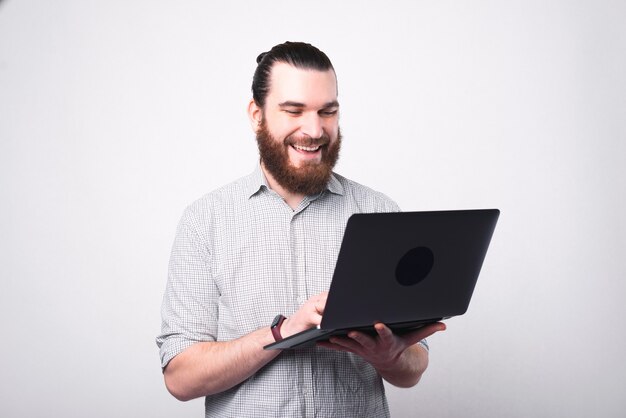 Portret van gelukkig bebaarde man in shirt met laptop over witte muur