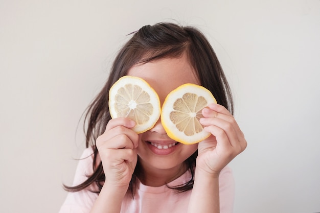 Portret van gelukkig jong meisje voor haar ogen met plakjes citroen, gezond eten levensstijl, veganistisch, plantaardig dieet, kind plezier met voedsel concept